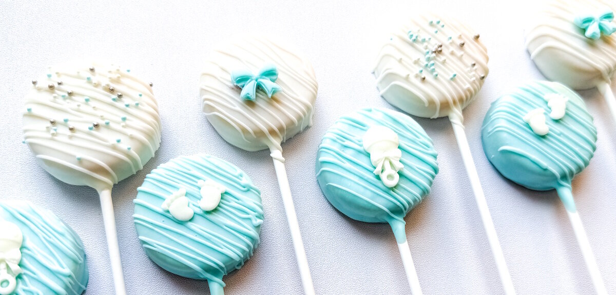 Baby shower cake pops in blue and white with drizzle, baby feet, bows, and rattles