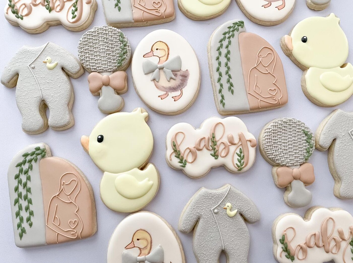 Duckling baby shower cookies in soft neutrals with watercolor ducks, rattles, and sleepers