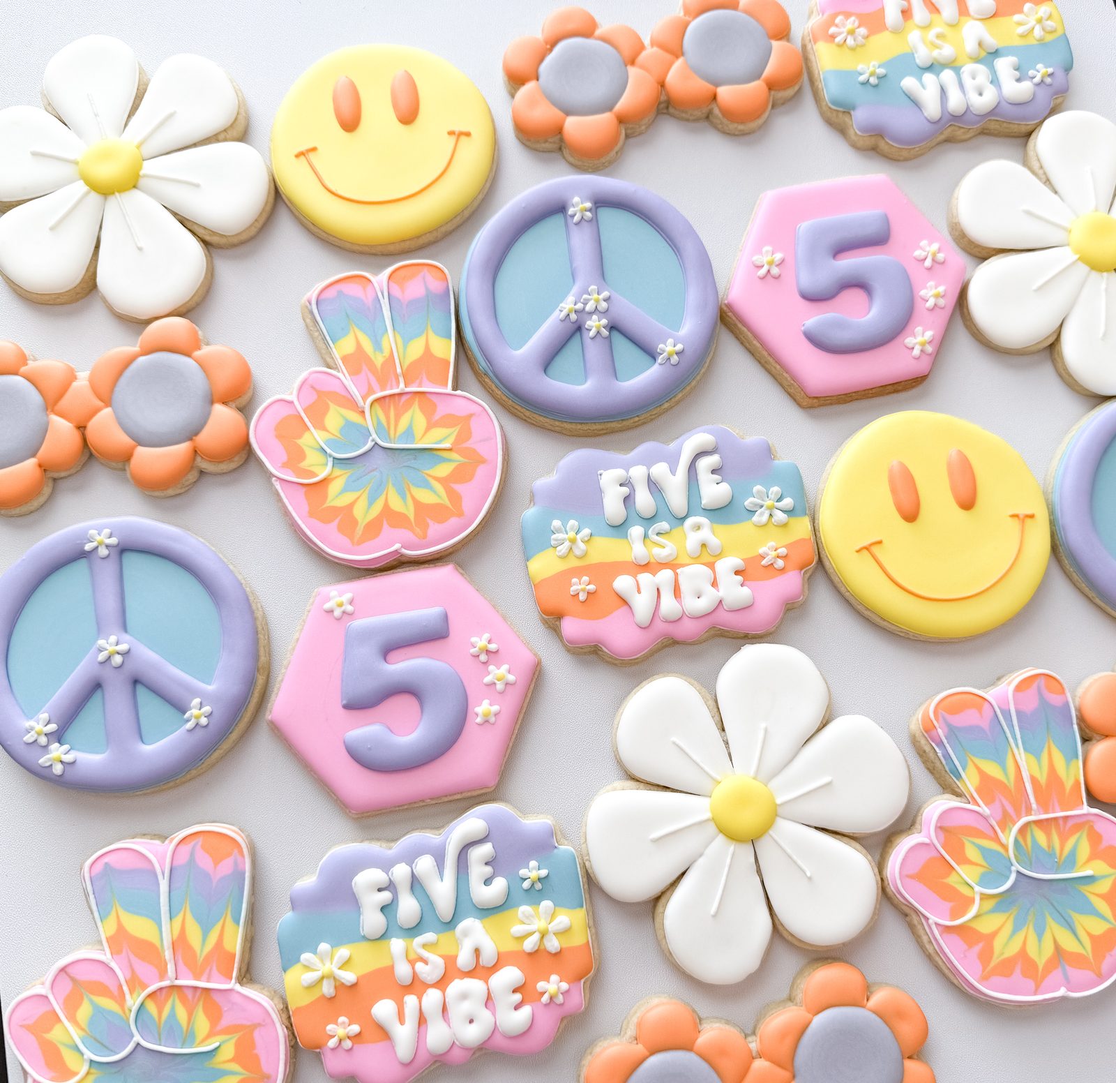 Five is a Vibe groovy birthday cookies with peace signs, smiley faces, daisies, and tie-dye