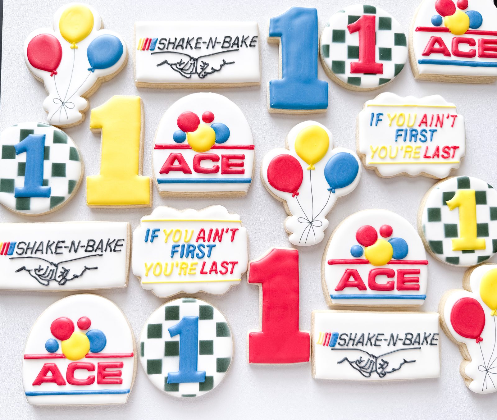 Racing themed first birthday cookies with Shake-N-Bake plaques, checkered flags, and balloons