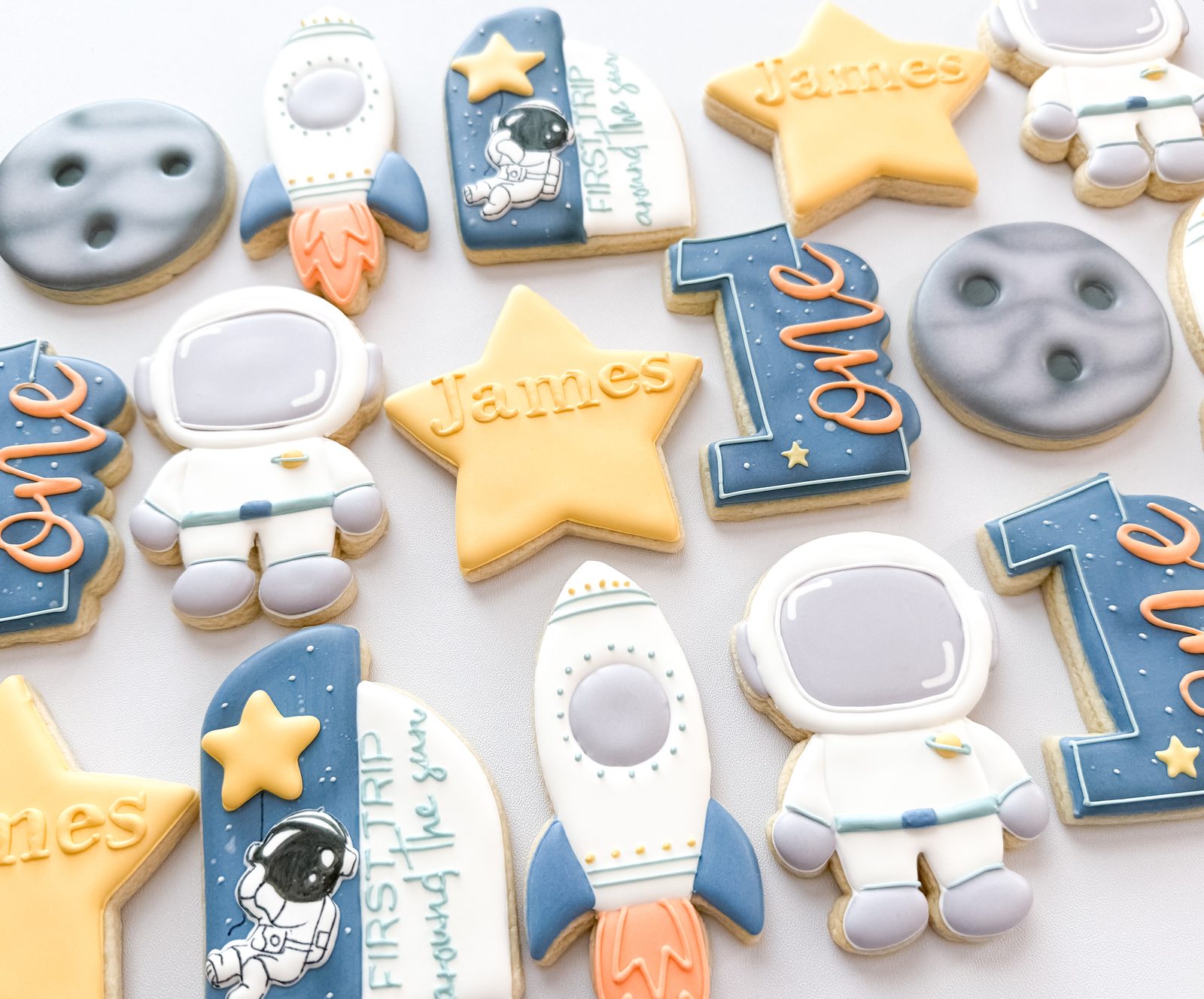 First Trip Around the Sun space birthday cookies with astronauts, rockets, moons, and name stars