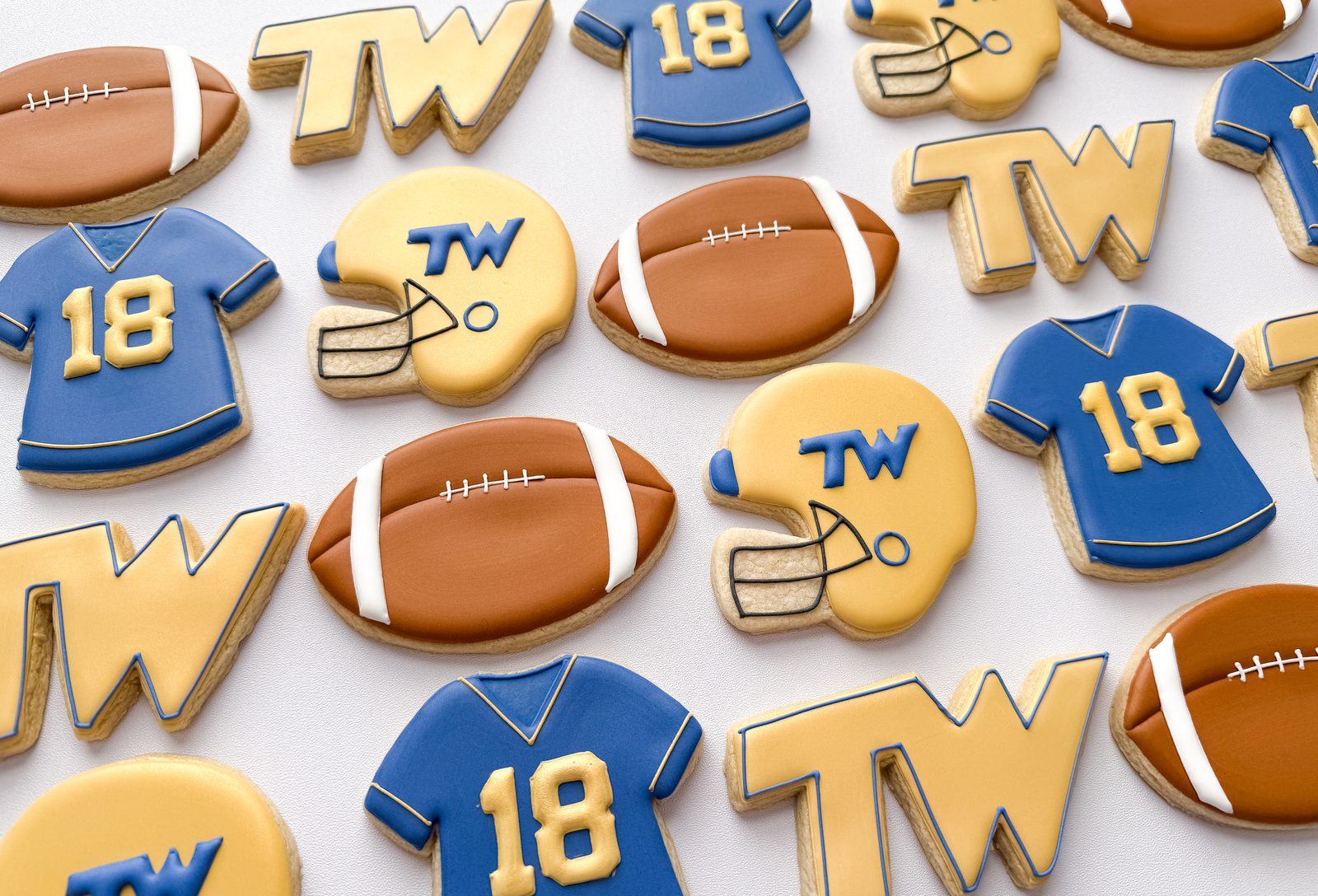 Football cookies in blue and gold with jerseys, helmets, footballs, and TW monograms