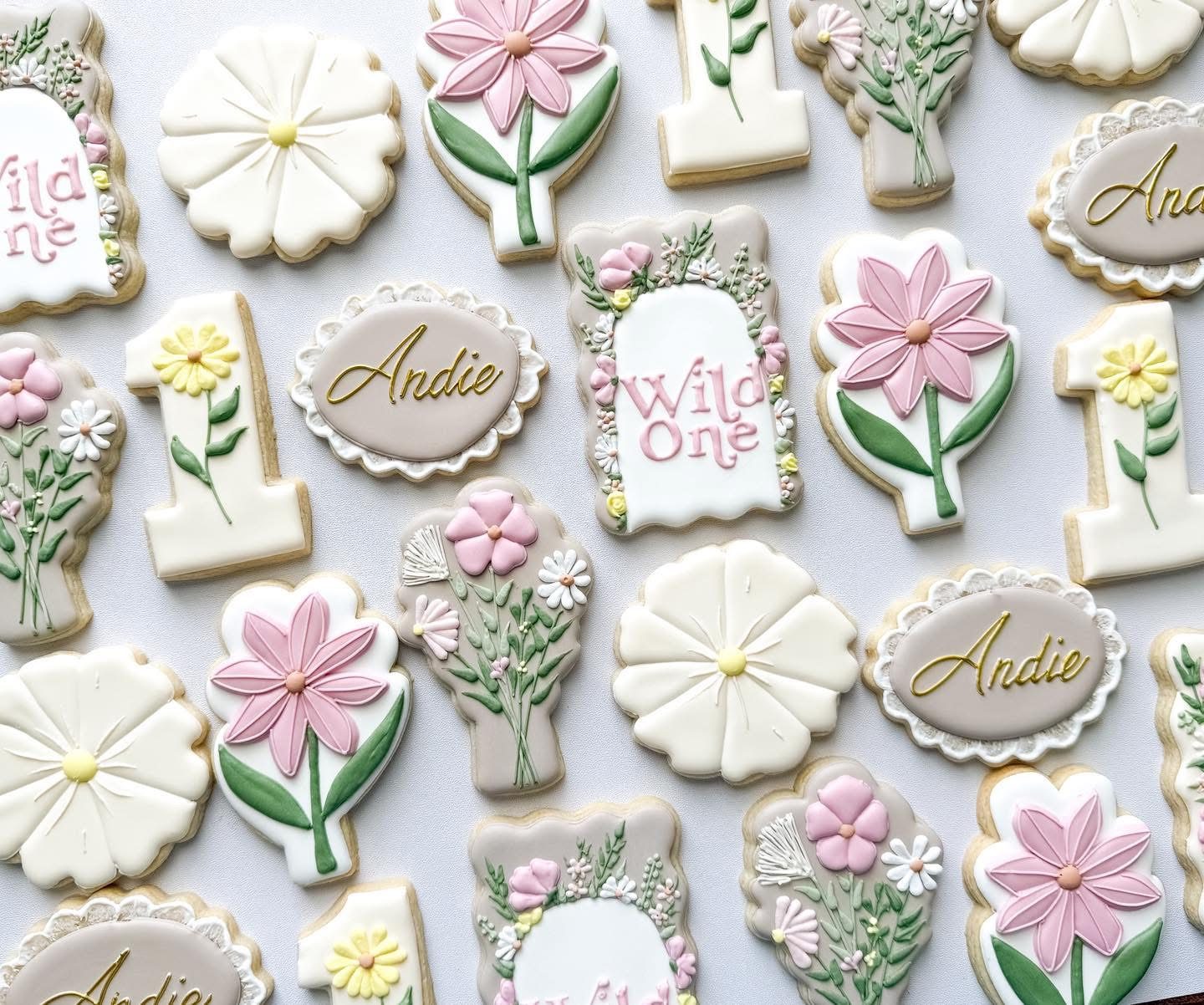 Wild One wildflower first birthday cookies with pink and yellow daisies, floral number ones, lace-edged name plaques, and Wild One lettering