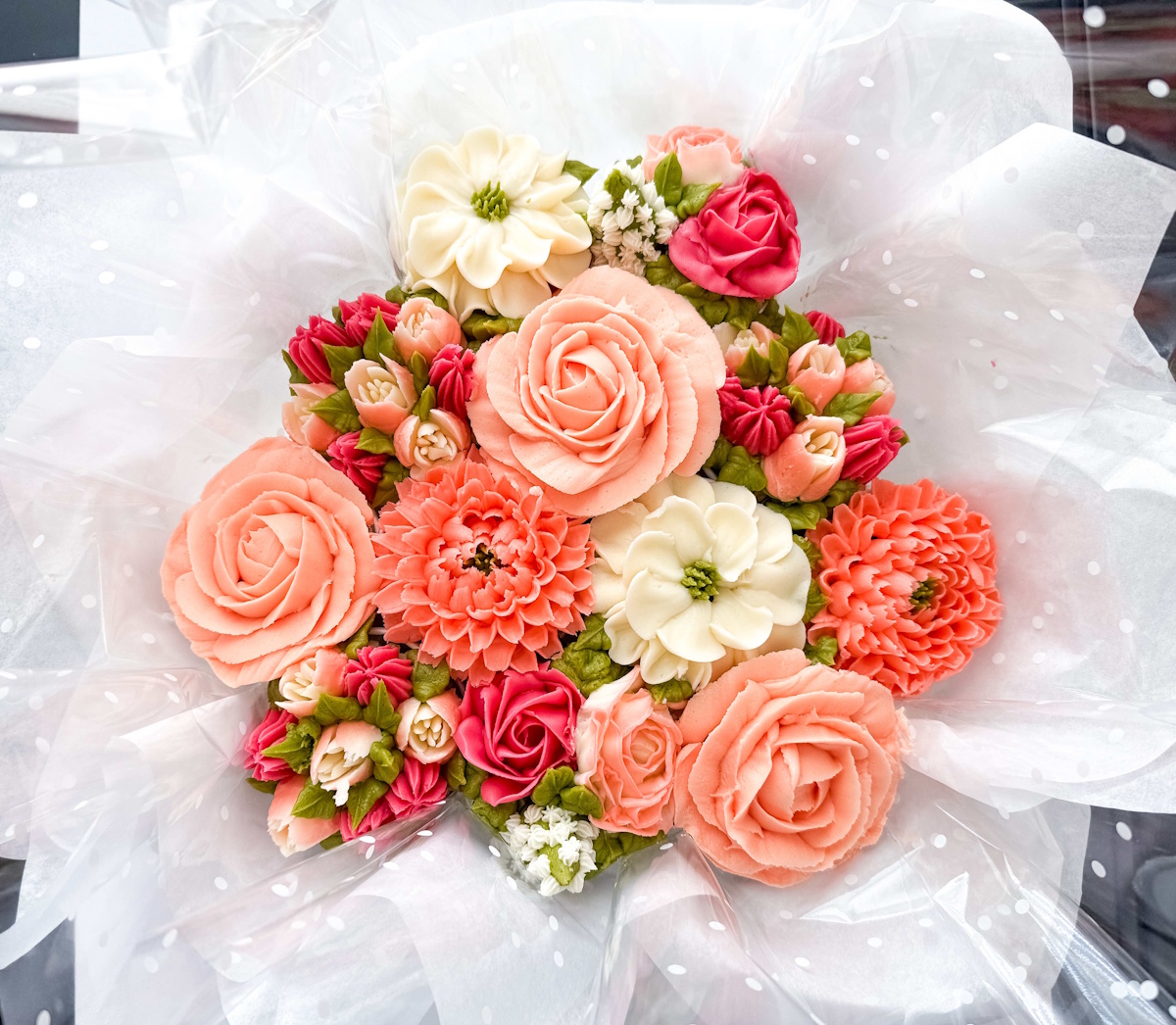 Buttercream cupcake bouquet with coral and cream roses, dahlias, and anemones wrapped like fresh flowers