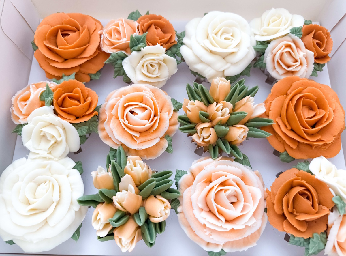 Boxed dozen buttercream flower cupcakes with terracotta, peach, and ivory roses and tulip bouquets